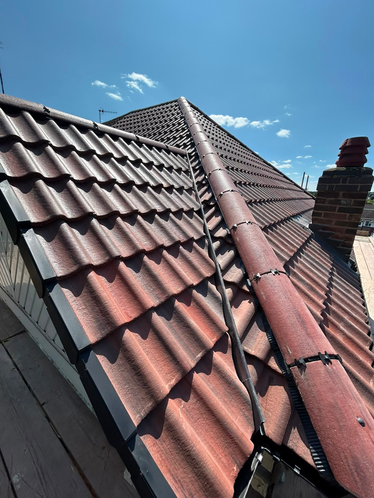 Red concrete roof tiles being secured with mechanical ridge clips