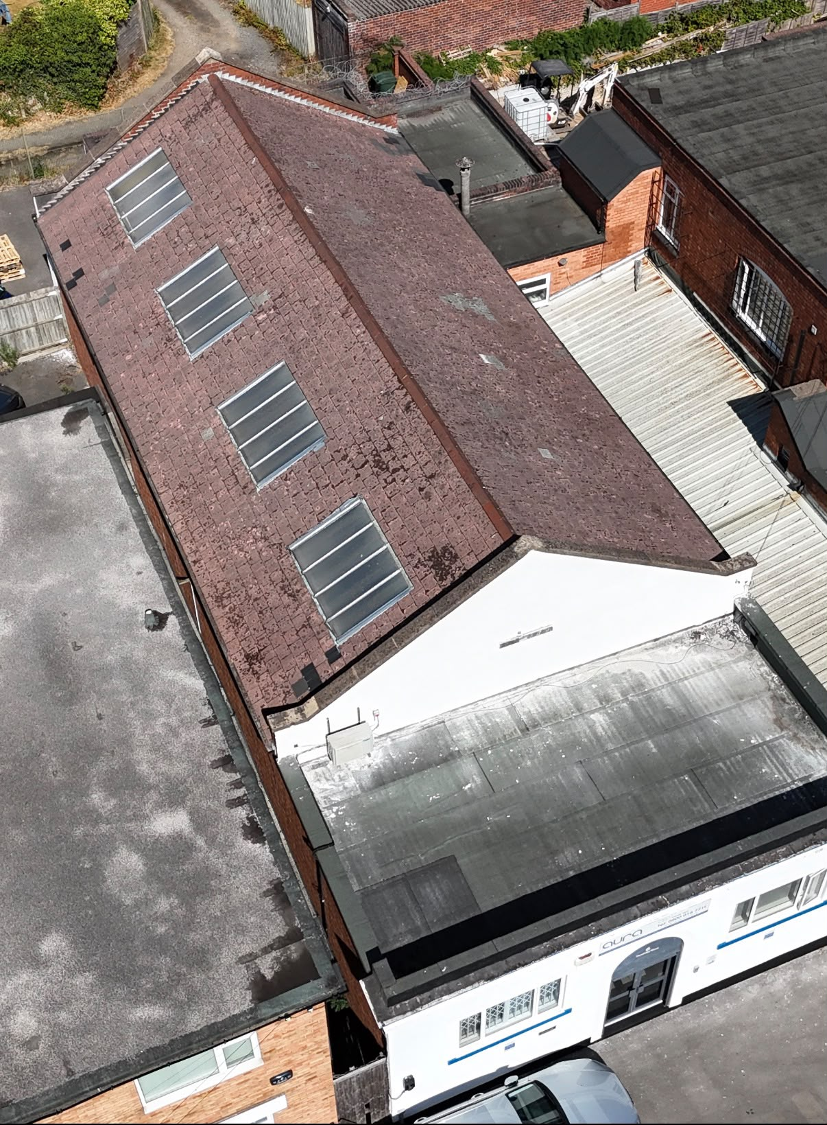 Aerial view of a worn, moss-stained tiled pitched roof with old rooflights on a commercial building in Coventry before re-roofing