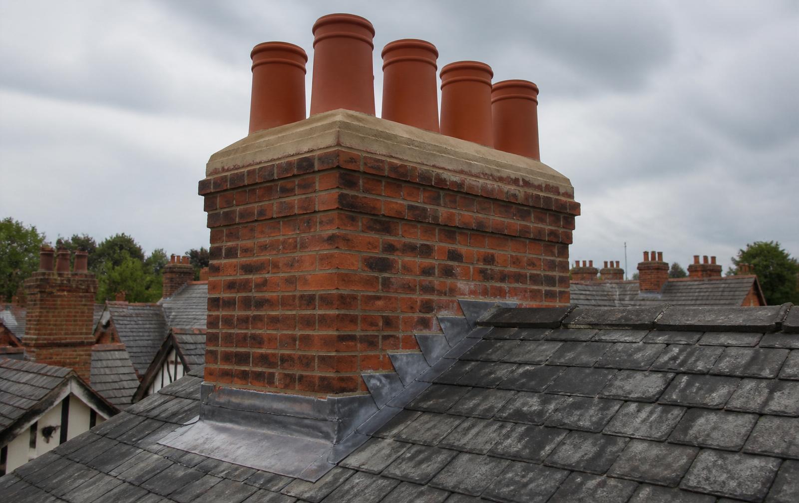 Rebuilt red-brick chimney stack with new terracotta pots, fresh flaunching and lead flashing on a British slate roof